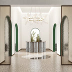 A round Clérachic chandelier on a gold ring hangs in a tall white entrance hall with green arches and patterned glass panels.