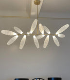 Close view of a linear Clérachic chandelier, its frosted white glass leaves on a gold rod against a grey wall.