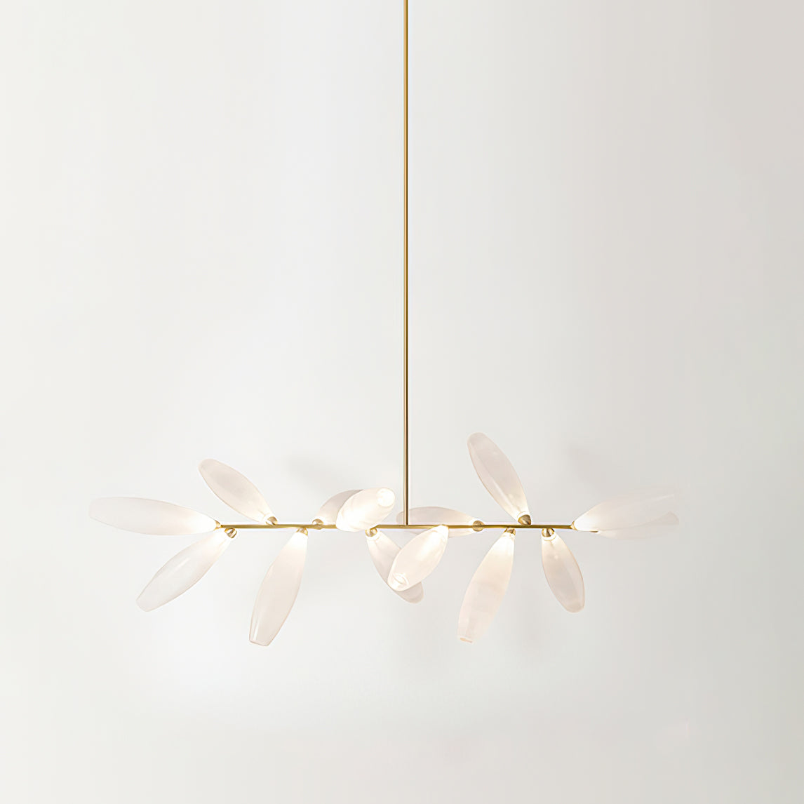 A linear Clérachic chandelier of frosted glass leaves hangs from a long gold rod against a pale backdrop, with a short cluster of leaves on each side.