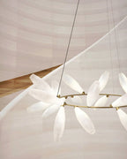 Close view of the round Clérachic chandelier, the gold ring and white glass leaves seen against a curved, pale wooden staircase.