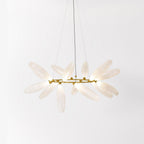 A round Clérachic chandelier with frosted white leaves fanning out from a gold ring, hung on three fine wires against a pale wall.