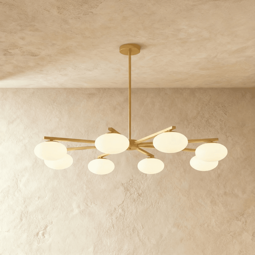 Clérachic eight-head chandelier with brushed brass arms and oval opal glass shades, glowing warmly on a limewash ceiling.