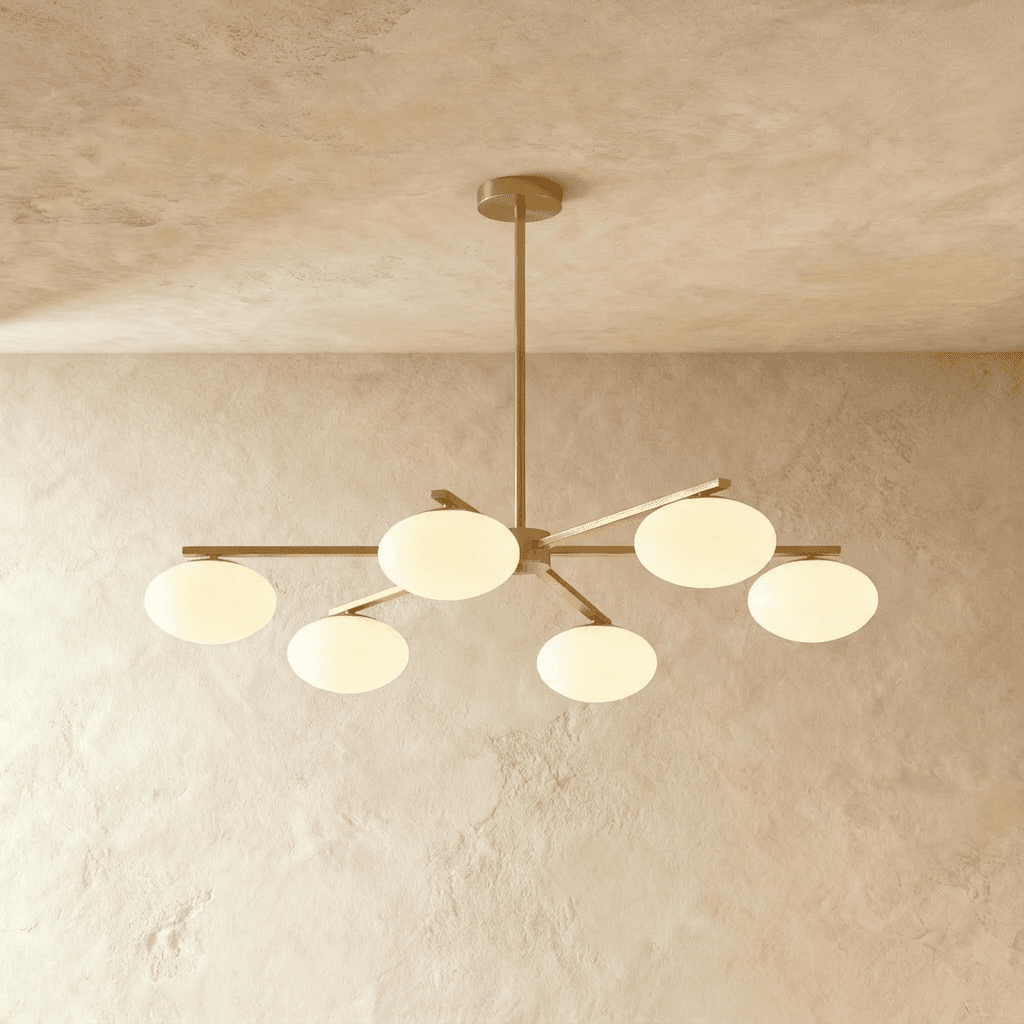 Clérachic six-head chandelier with slim brass arms and rounded opal glass shades, hung from a short stem in a plaster-walled room.