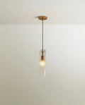 Clérachic slim pendant, a clear glass cylinder with a brass fitting and black cord hanging below a plain ceiling canopy.