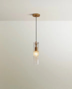 Clérachic slim pendant, a clear glass cylinder with a brass fitting and black cord hanging below a plain ceiling canopy.