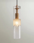Clérachic pendant close-up, a clear glass cylinder around a brass holder and a frosted pebble-textured band, lit warm.