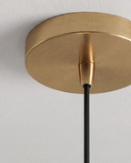 Clérachic pendant detail, a round brushed brass ceiling canopy and cord grip with a slim black cord hanging below.