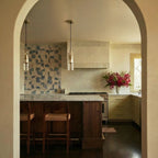Clérachic clear glass cylinder pendants in pairs with brass fittings, hung above a kitchen island and patterned tiles.