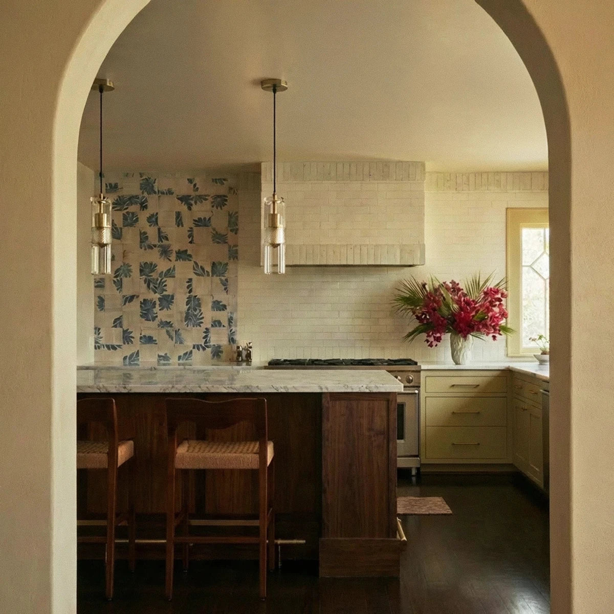 Clérachic clear glass cylinder pendants in pairs with brass fittings, hung above a kitchen island and patterned tiles.