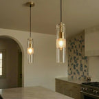 Clérachic glass cylinder pendants with brass holders and glowing frosted bands, hanging in a warm kitchen beside an arch.