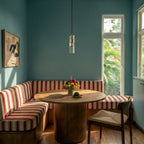 Clérachic slim glass cylinder pendant over a round wooden table in a teal dining nook with striped banquette seating.