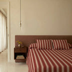 Clérachic slim glass cylinder pendant hung beside a bed with a floating walnut nightstand and red striped bedding.