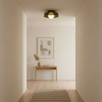 Looking down a pale hallway, a small Clérachic glass-disc ceiling light with a white globe sits above a console and a framed print.