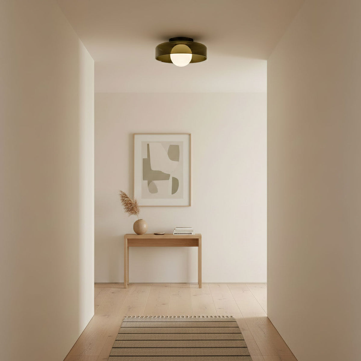 Looking down a pale hallway, a small Clérachic glass-disc ceiling light with a white globe sits above a console and a framed print.