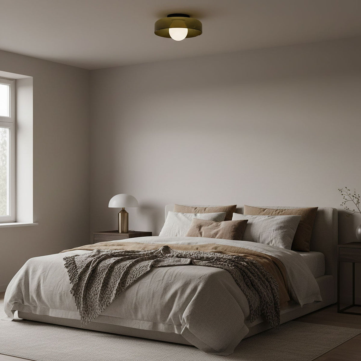 In a bedroom with a window and neutral bedding, a Clérachic glass-disc ceiling light sits above the bed with its globe lit.