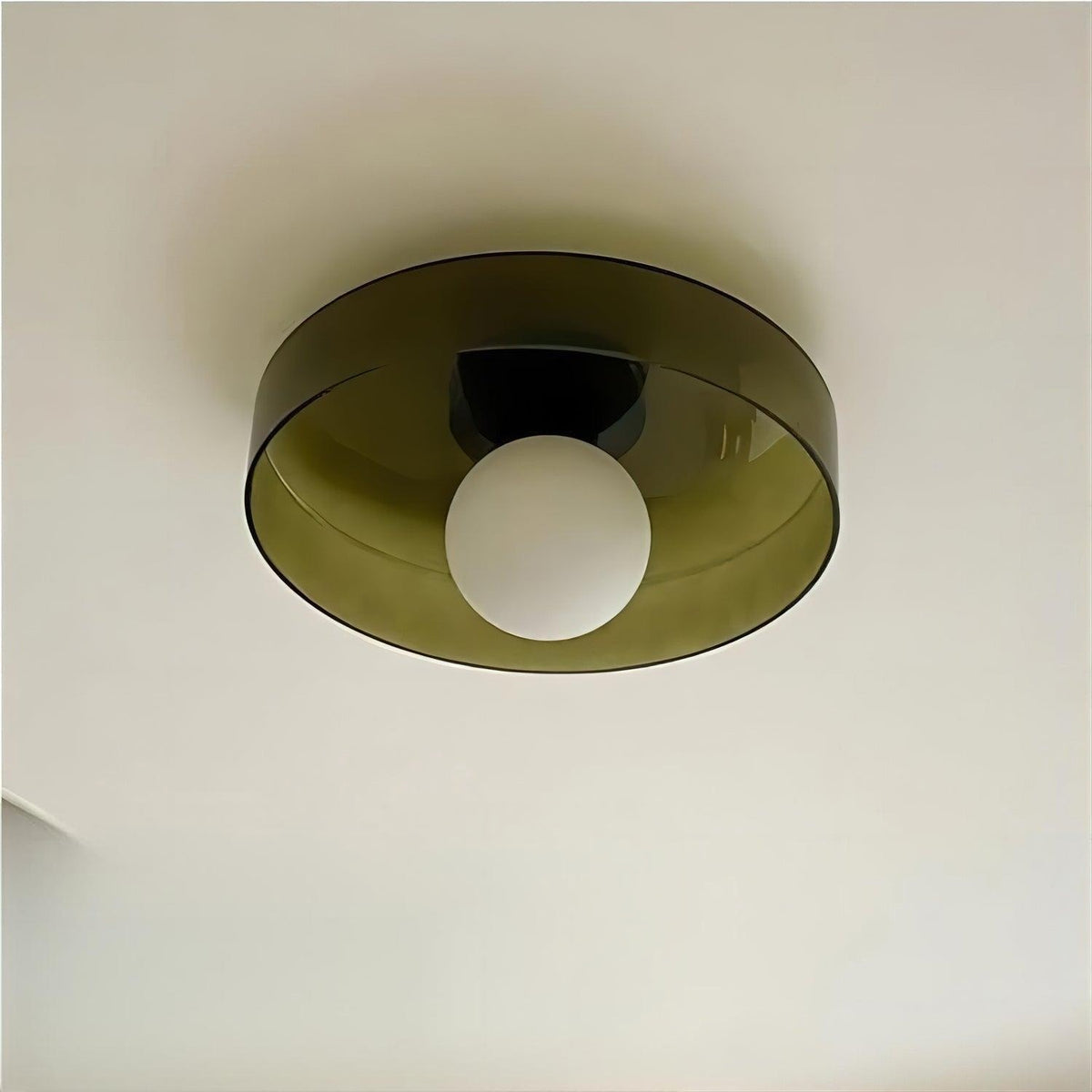 Underside of an olive-brown Clérachic glass disc with a frosted white globe, against a cream ceiling.