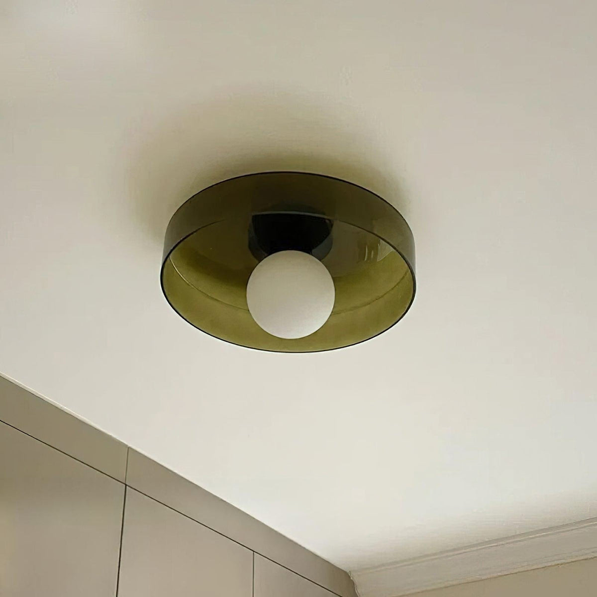 Seen from below, this Clérachic ceiling light has an olive smoked glass disc, a black plate and a frosted white globe.