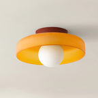Close view of a Clérachic ceiling light with an amber-orange glass disc, a deep red mounting plate and a white globe.