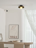 This Clérachic glass-disc ceiling light sits above a curved white wall, with a framed print and a pale table below.