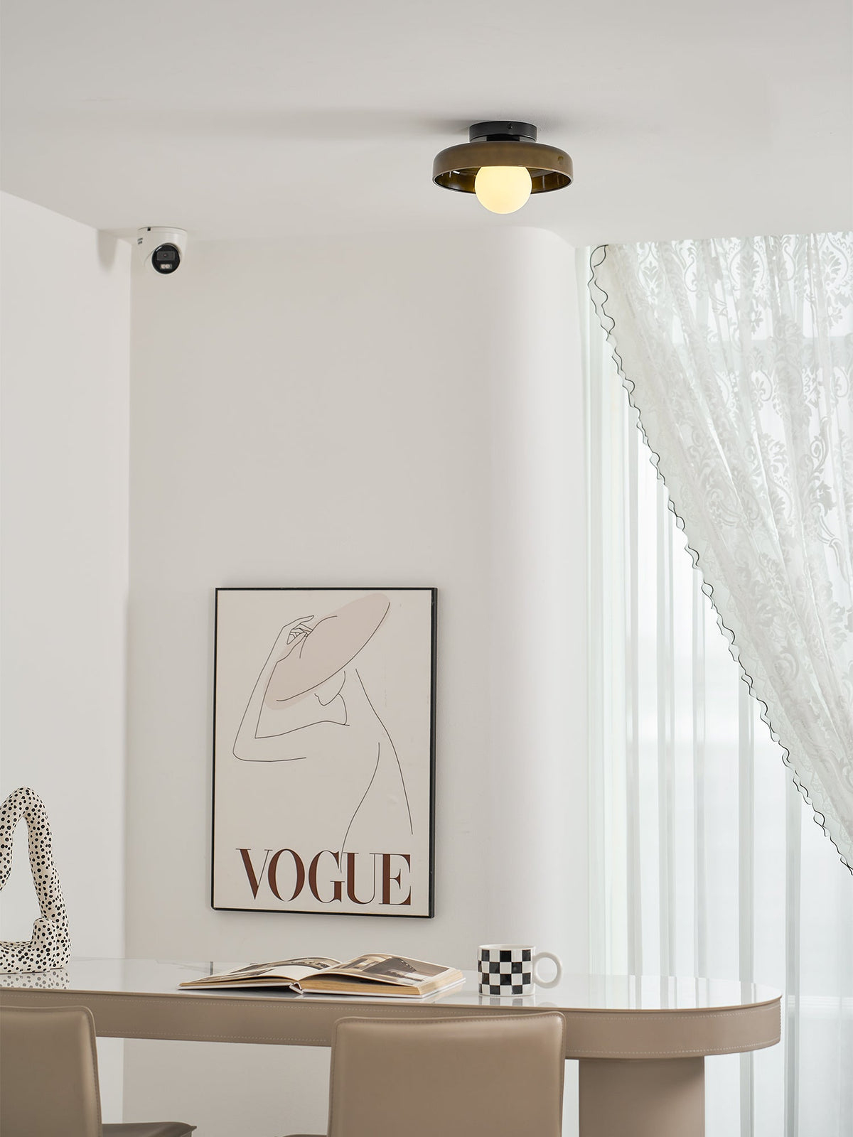 This Clérachic glass-disc ceiling light sits above a curved white wall, with a framed print and a pale table below.
