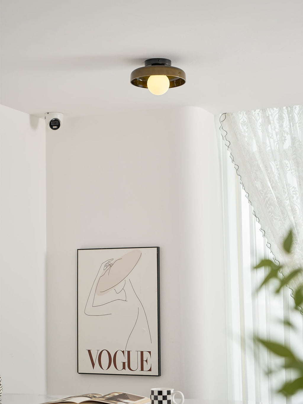 Seen higher in the room, a Clérachic glass-disc ceiling light sits above a framed print and a green plant leaf.