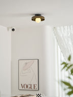 Seen higher in the room, a Clérachic glass-disc ceiling light sits above a framed print and a green plant leaf.