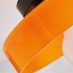 Close view of the rim of an amber-orange glass disc from Clérachic, with the white globe partly visible behind it.