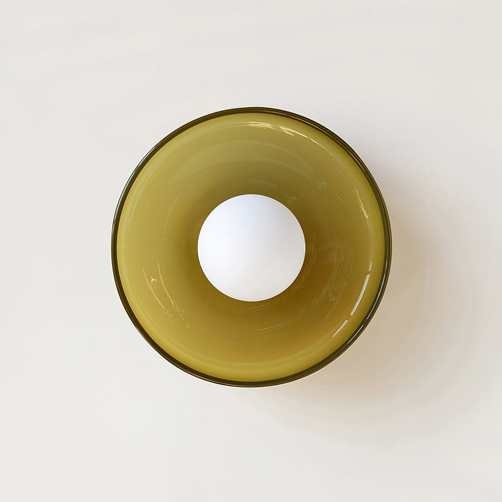 An olive glass-disc light from Clérachic seen head-on, mounted on a cream wall with the white globe unlit.
