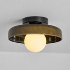 Side view of the Clérachic olive-brown glass-disc light, its white globe glowing warm under the rim against a grey ceiling.