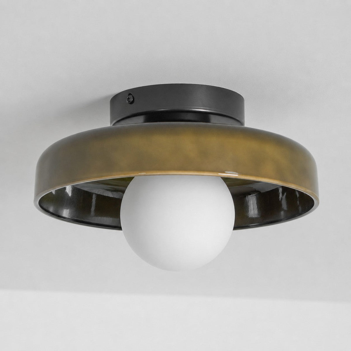 An unlit Clérachic ceiling light with a bronze-olive glass disc, a black plate and a white globe, on a grey ceiling.