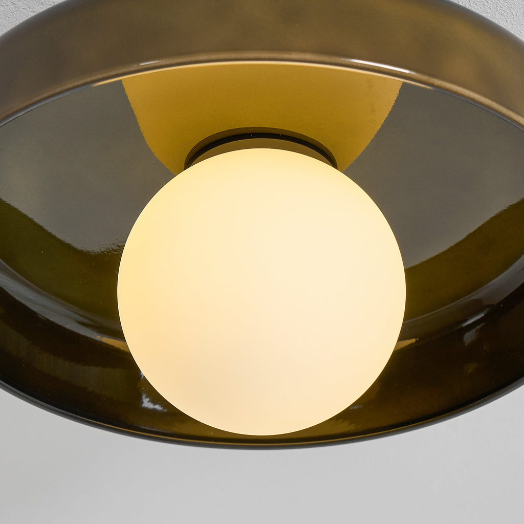 Close view of the lit white globe glowing inside the olive glass disc of this Clérachic ceiling light.