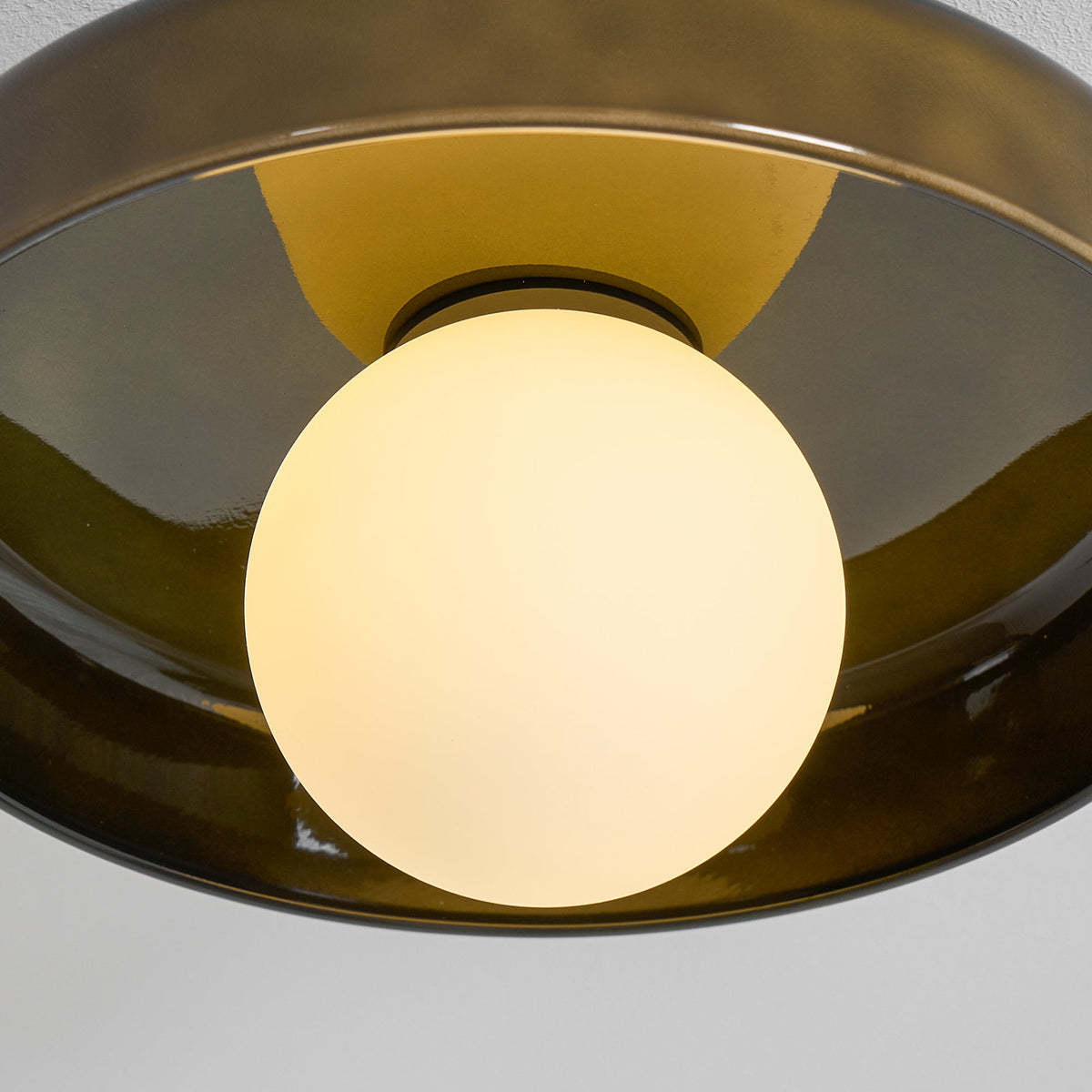Close view of the lit white globe glowing inside the olive glass disc of this Clérachic ceiling light.