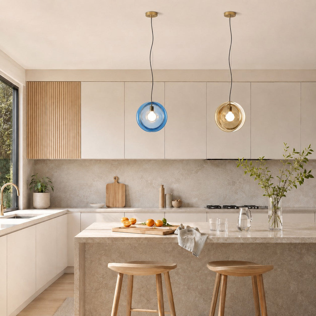 Two Clérachic glass pendants, one light blue and one amber, hang over a kitchen island with two pale wood stools.