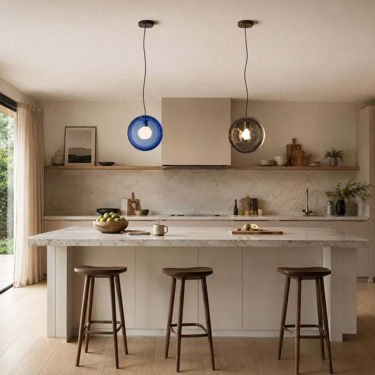 A dark blue and a smoky grey Clérachic glass pendant above a stone-topped island, with three tall wooden stools and open shelves.
