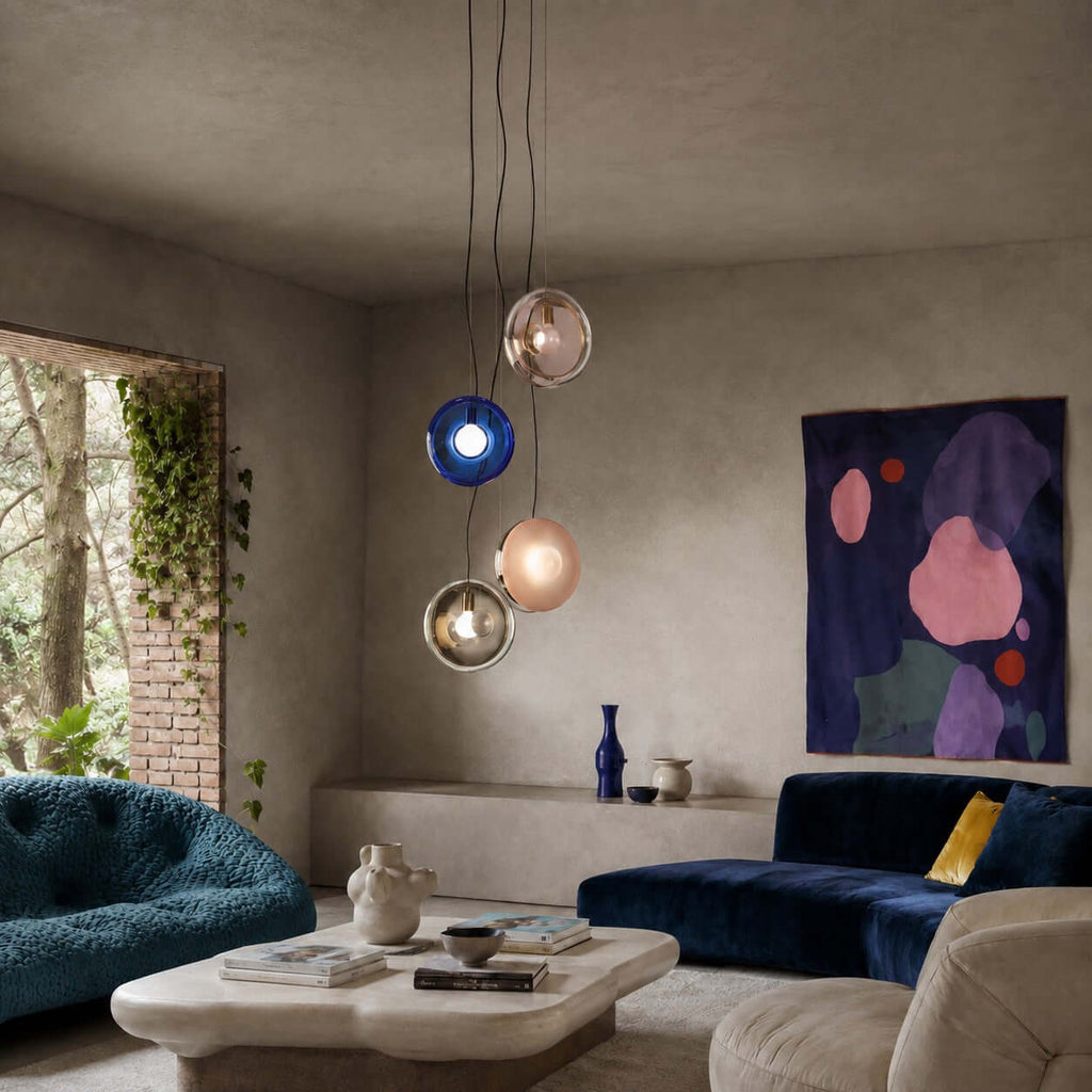 Cluster of Clérachic glass pendants in dark blue, pink and clear hung low over a coffee table in a living room with a navy sofa.