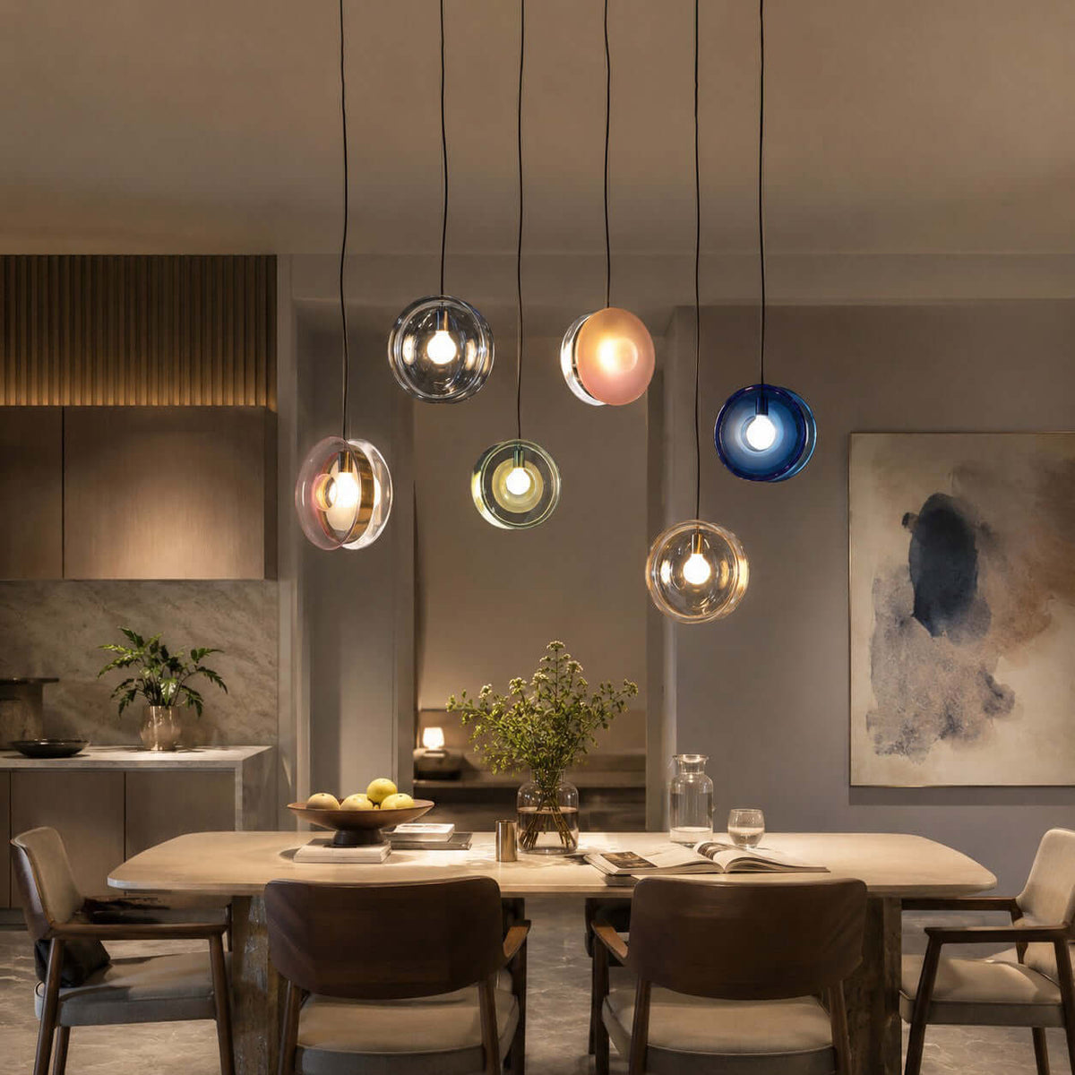 Six Clérachic glass pendants in mixed colours hung at varied heights over a long dining table with dark wood chairs.