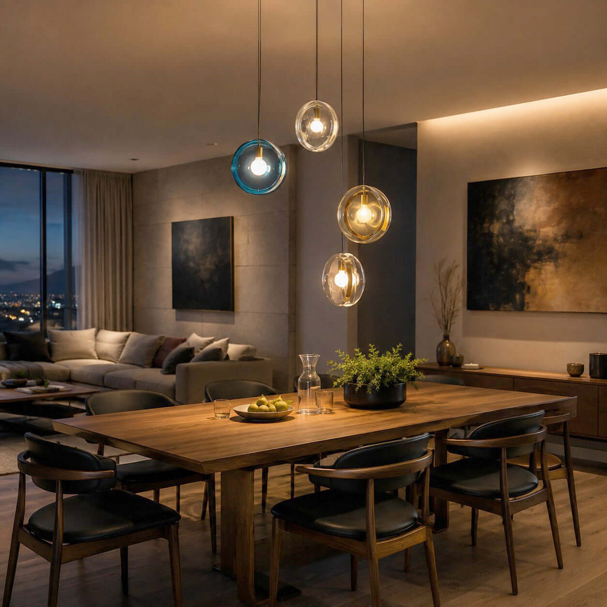 Lit Clérachic glass pendants in light blue, clear and amber over a wooden dining table, with a dusk city view beyond a window.