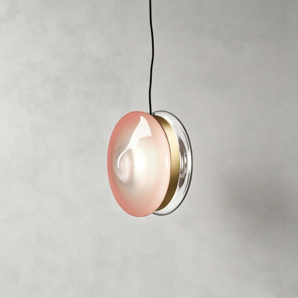 Clérachic glass disc pendant in soft pink glass with a brass band and a clear rim, hanging from a black cord.