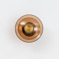 Front view of a Clérachic wall light with a round amber glass disc, a smaller inner dish and a gold centre cap.