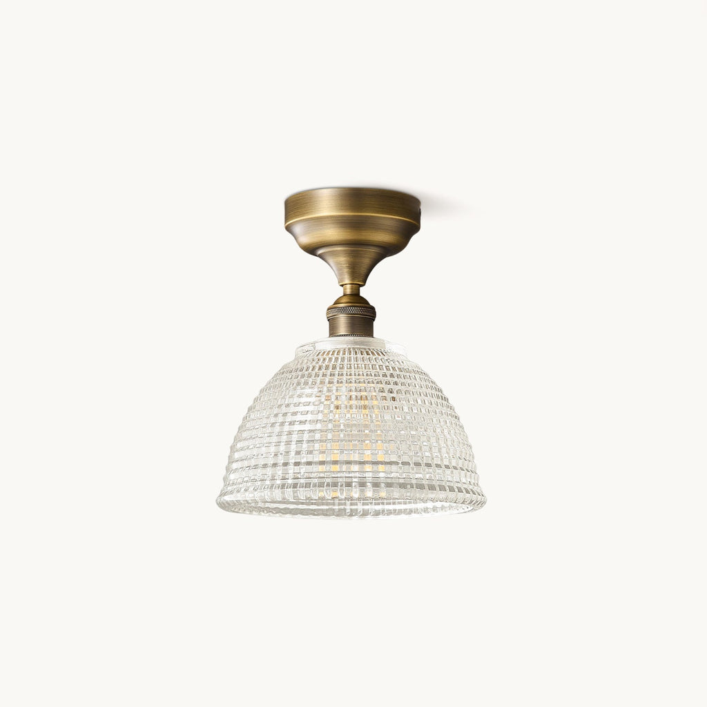 A Clérachic semi-recessed ceiling light with an antique brass canopy and a clear ribbed glass dome, on a plain off-white backdrop.