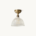 A Clérachic semi-recessed ceiling light with an antique brass canopy and a clear ribbed glass dome, on a plain off-white backdrop.