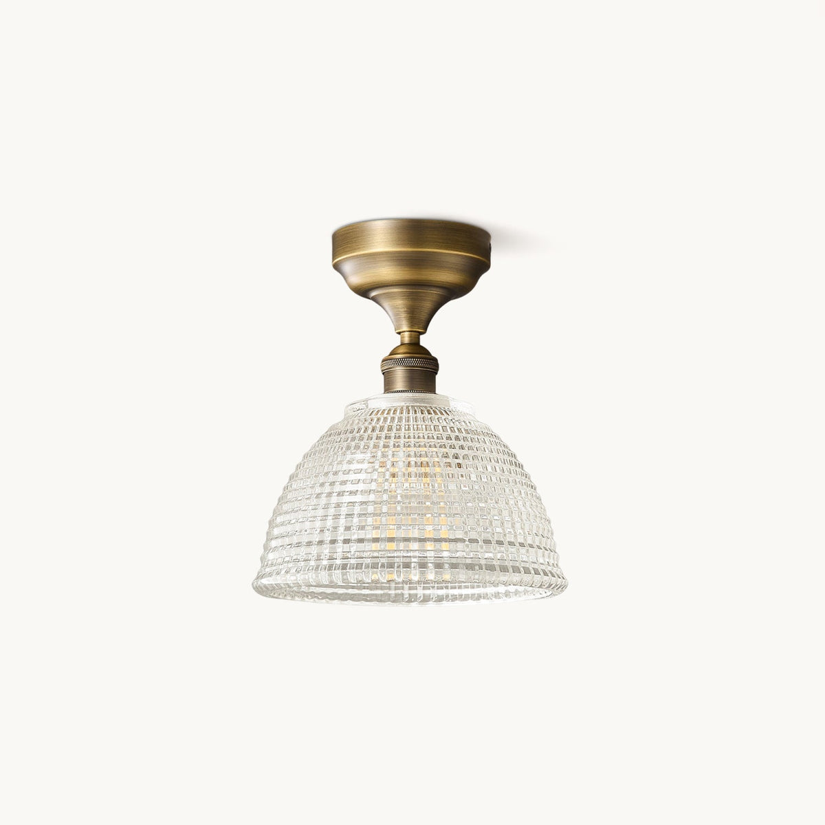 A Clérachic semi-recessed ceiling light with an antique brass canopy and a clear ribbed glass dome, on a plain off-white backdrop.