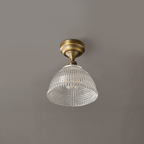 An unlit Clérachic ceiling light with a clear grid-patterned glass dome and antique brass fitting, against a grey ceiling.