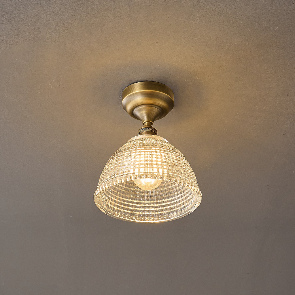 Switched on, this Clérachic ceiling light lets warm light through its clear grid-cut glass dome beneath an antique brass canopy.