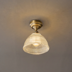 Switched on, this Clérachic ceiling light lets warm light through its clear grid-cut glass dome beneath an antique brass canopy.