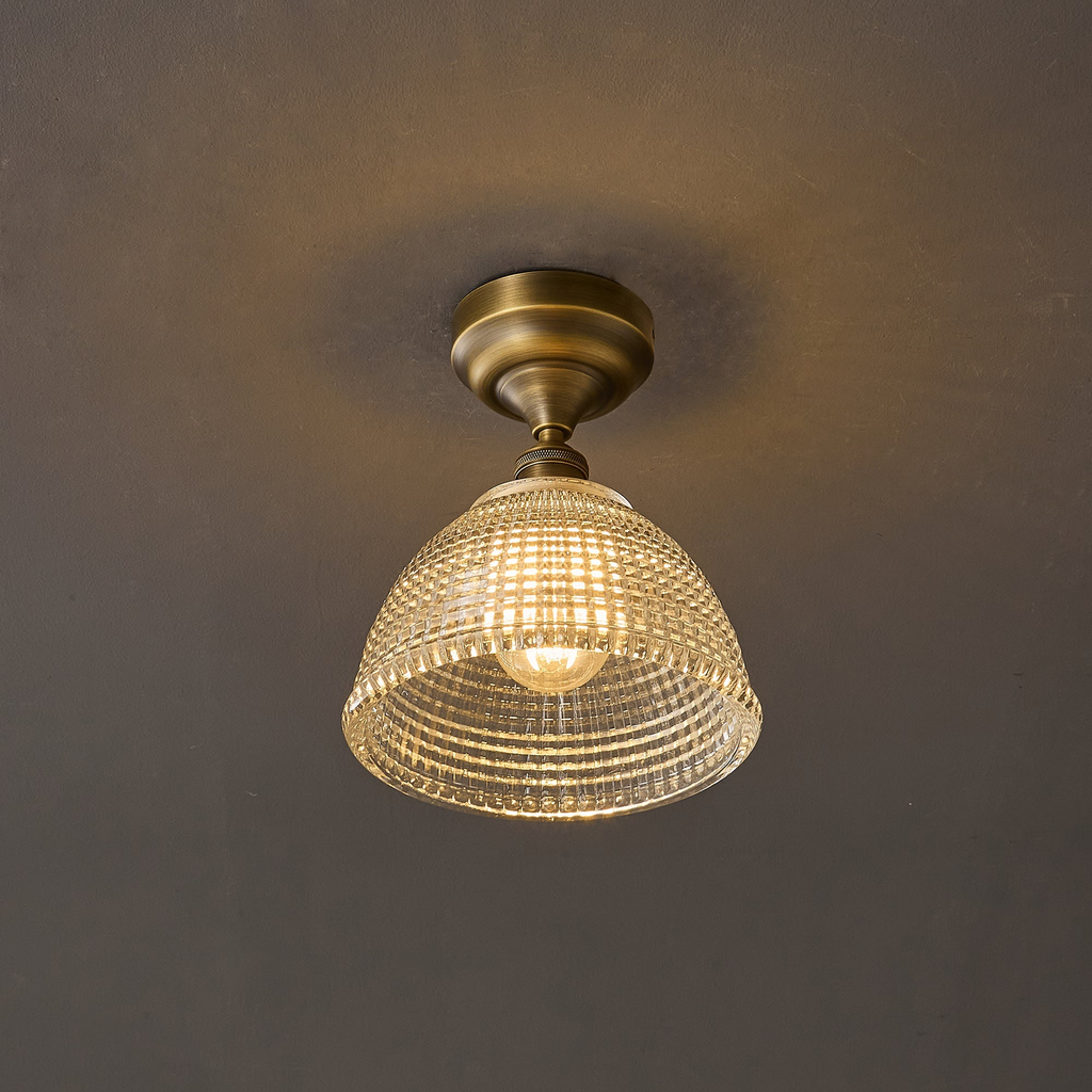 Lit warm against a dark grey ceiling, this Clérachic fitting shows its glass dome glowing with a visible bulb inside.