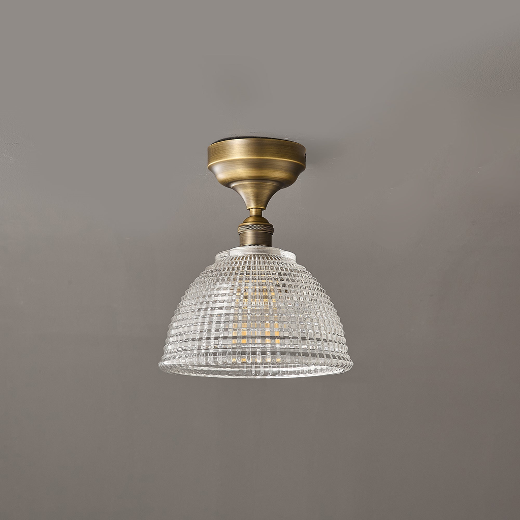 Unlit, the clear grid-patterned glass dome of this Clérachic ceiling light hangs from a short antique brass stem.