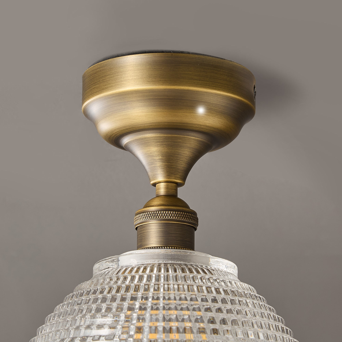 Close view of the antique brass canopy and knurled collar on this Clérachic ceiling light, above the top of the glass dome.