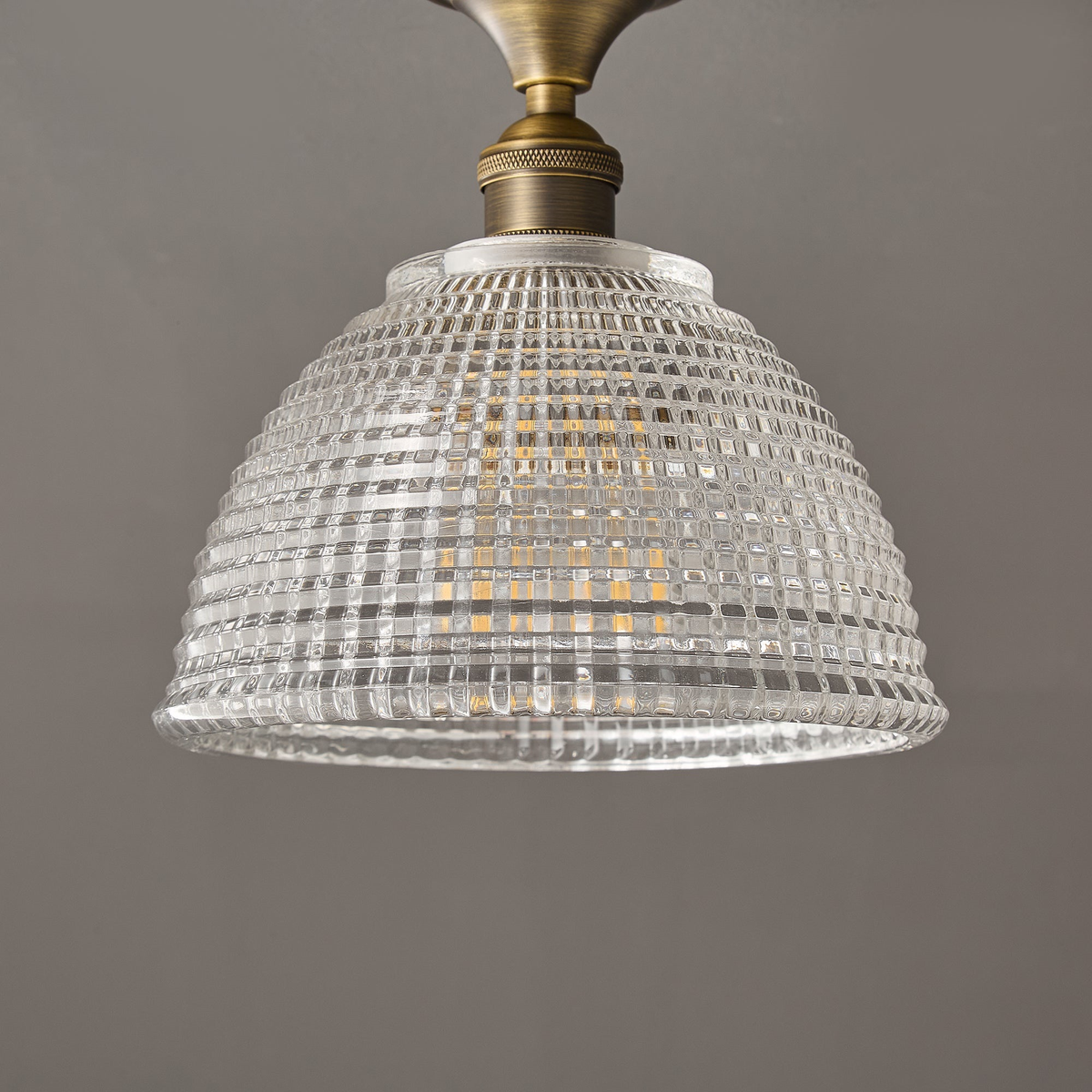 The clear ribbed glass dome of this Clérachic ceiling light, seen from below with its brass stem and white collar at the top.