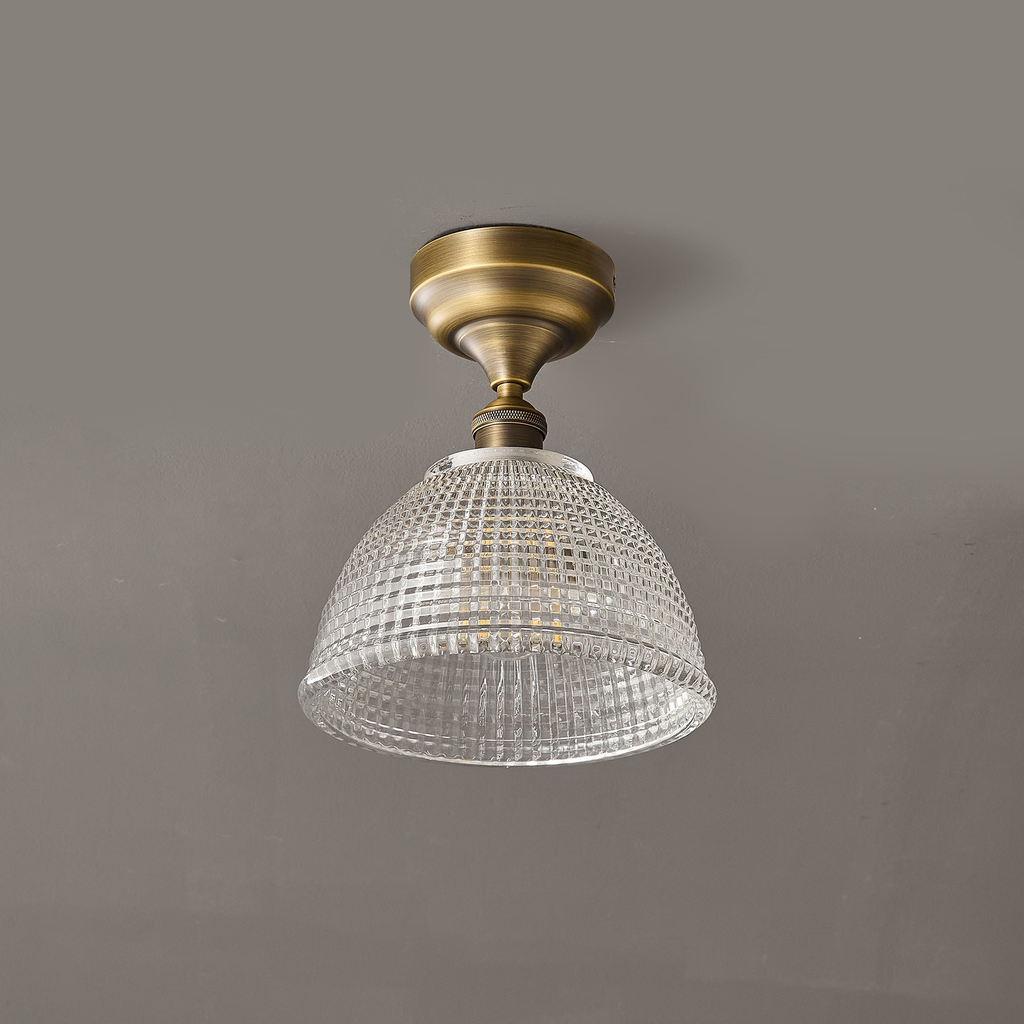 A Clérachic ceiling light seen straight on against a grey ceiling, the clear glass dome hanging below a round brass canopy.
